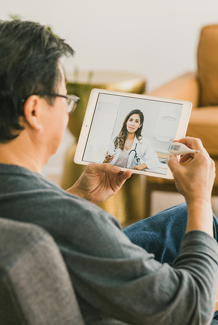 A man sits with a tablet and a thermometer during a virtual visit with his doctor.