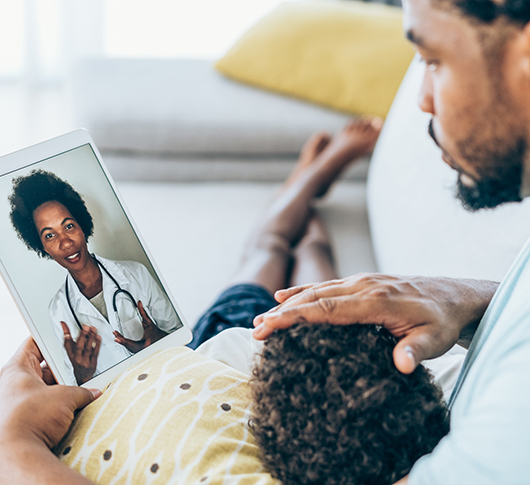 A father consoles his sick baby while talking to a doctor during a virtual visit.
