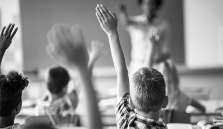 Kids in a classroom with hands raised