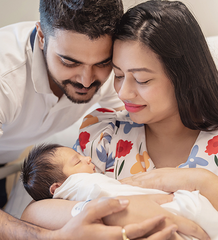 A mother and father smile as they hold and look down at their newborn baby.
