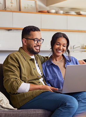 A couple sit on couch and type on laptop and registers for a Blue Cross online account.