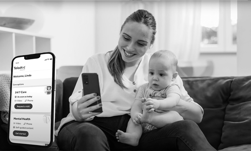 A woman smiles as she holds her baby on her knee and looks on her phone.