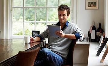 A man looking at tablet while drinking coffee at the dining room table