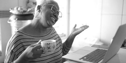 Woman smiling holding a coffee mug talking to her laptop.