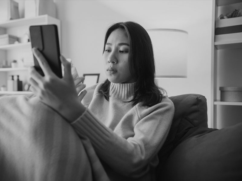 Young woman using smart phone that is resting on her knee.