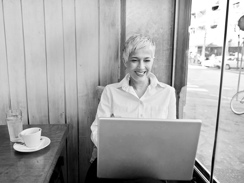 Woman on laptop in a restaurant, near a window.