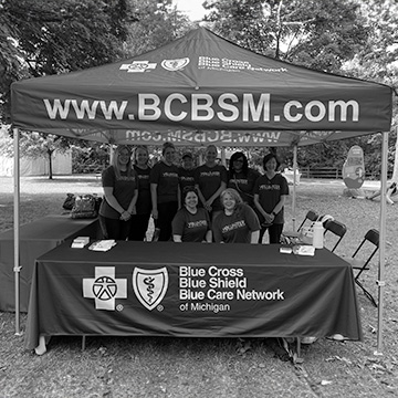 Blue Cross volunteers stand under a tent at an event.