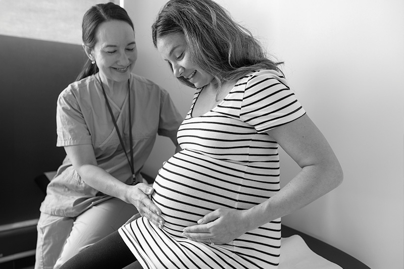 A pregnant woman smiles while she gets care from her doctor. 