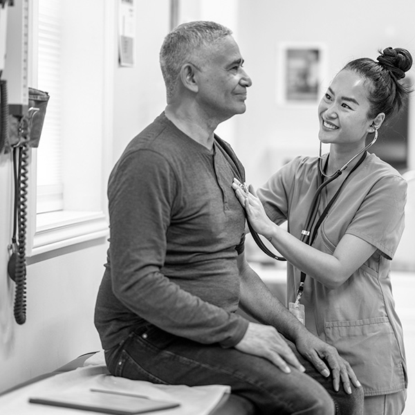 A man sits as a doctor uses a stethoscope to listen to his heart.