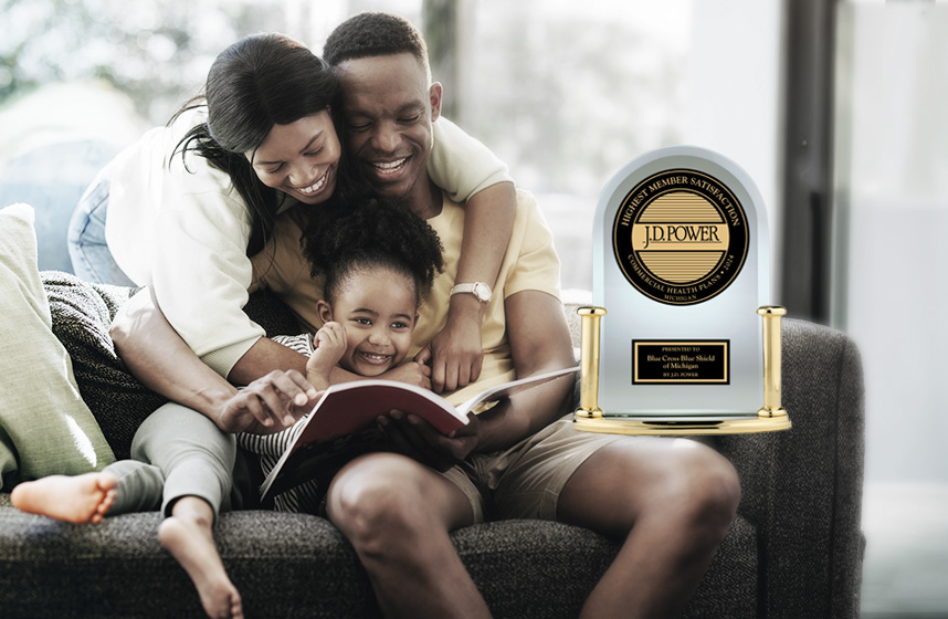 Woman, man and child sit on couch smiling reading a book