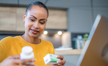 A woman looks at her medicine while she uses her laptop.